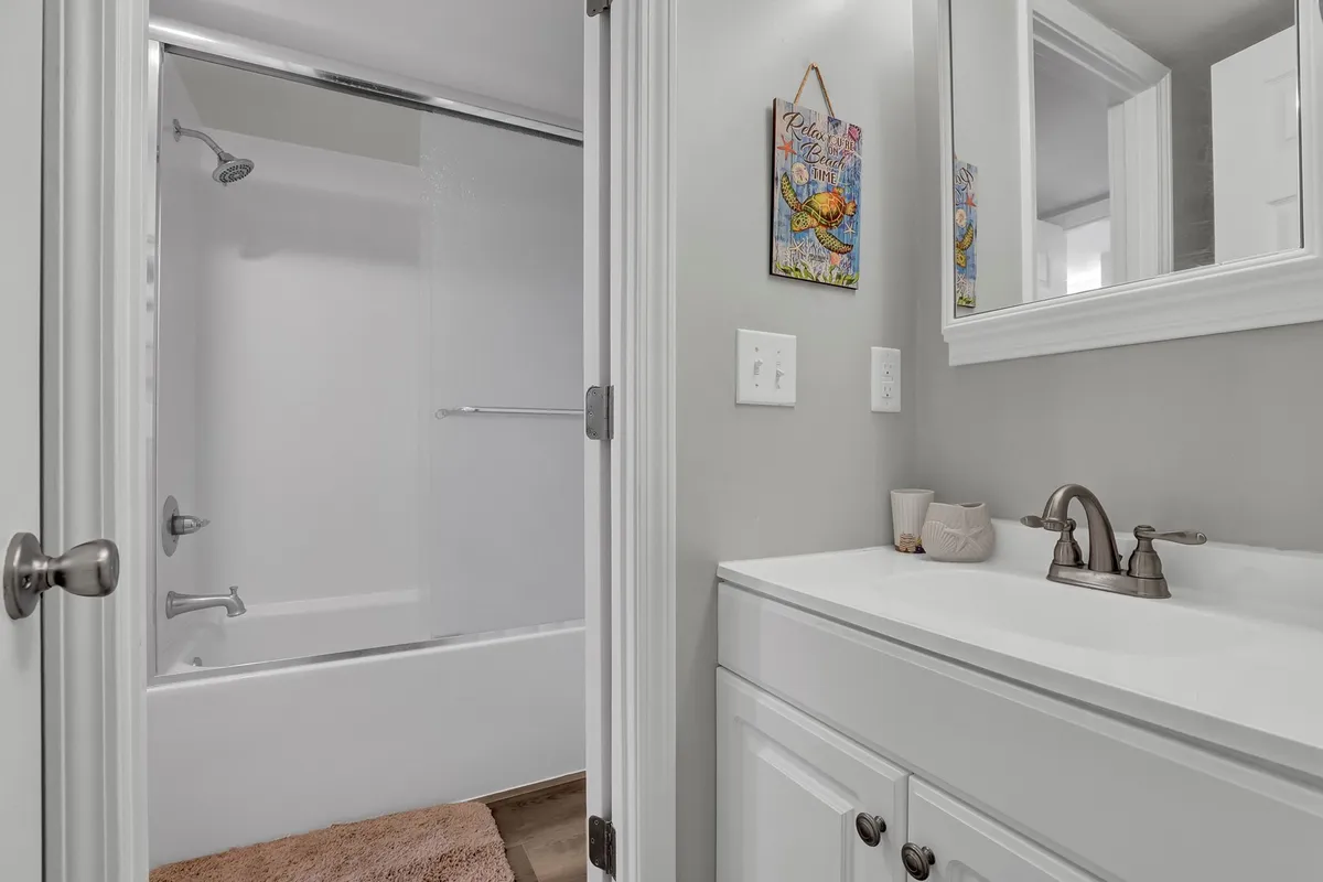 A bright, clean bathroom featuring a vanity sink with a mirrored cabinet, a shower area, and decorative wall art. The atmosphere is refreshing and practical, with enough space for personal routines and group convenience.