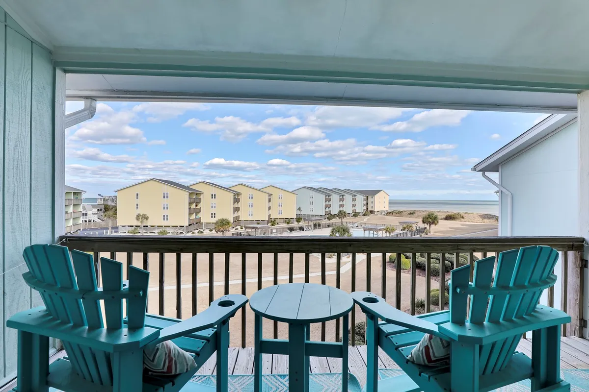 An inviting private balcony featuring a pair of Adirondack chairs and a small table, with a direct view of the ocean stretching out beyond the railing. The setting suggests a tranquil, pet-friendly spot where guests can relax with their pets and soak in the sea breeze together after a day of adventure.