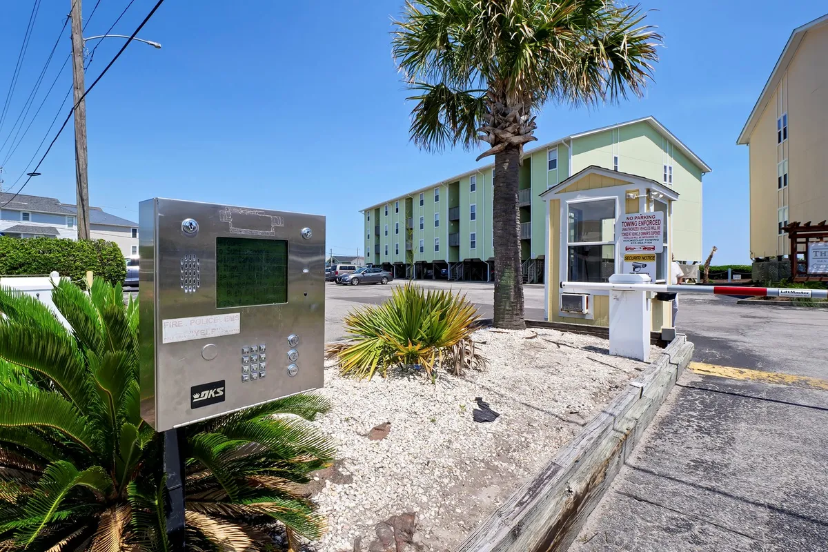 This image shows the exterior facade of the building, with palm trees and an intercom system near the entrance. The scene captures the initial arrival experience, highlighting the welcoming vibe and ease of access to local amenities and the neighborhood.