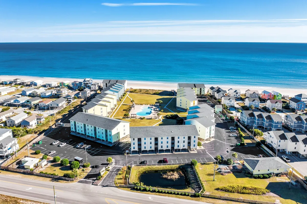 A vibrant exterior view featuring an inviting swimming pool surrounded by green spaces and colorful buildings, all set against the backdrop of a sweeping ocean view. The layout highlights communal outdoor areas ideal for social gatherings and relaxation.