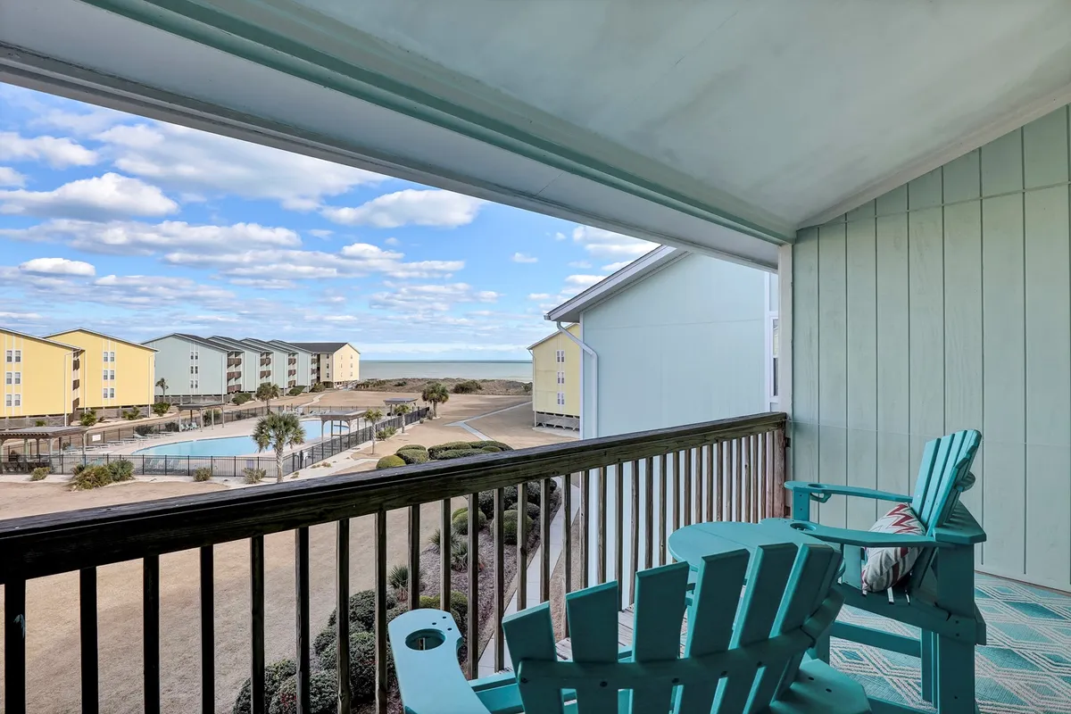 An inviting balcony view that overlooks the community pool and features colorful buildings in the background. The scene conveys the pleasure of relaxing on the balcony, watching children play in the pool, or gathering for a casual evening barbecue.